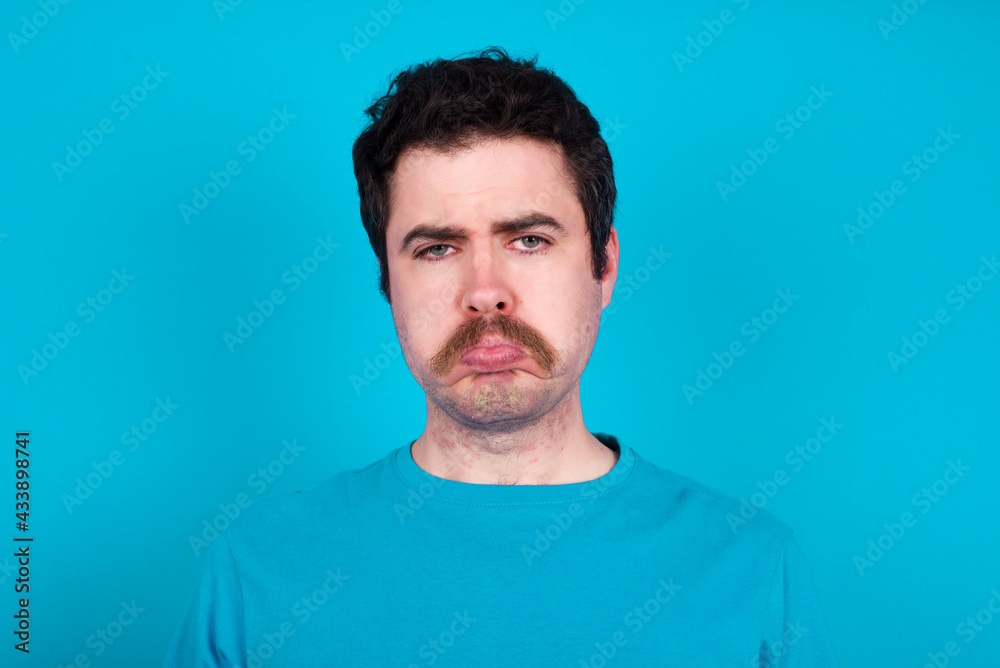 young handsome Caucasian man with moustache wearing blue t-shirt against blue background depressed and worry for distress, crying angry and afraid. Sad expression. young handsome Caucasian man with moustache wearing blue t-shirt against blue background depressed and worry for distress, crying angry and afraid. Sad expression.