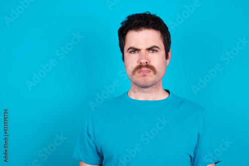 young handsome Caucasian man with moustache wearing blue t-shirt against blue background Pointing down with fingers showing advertisement, surprised face and open mouth