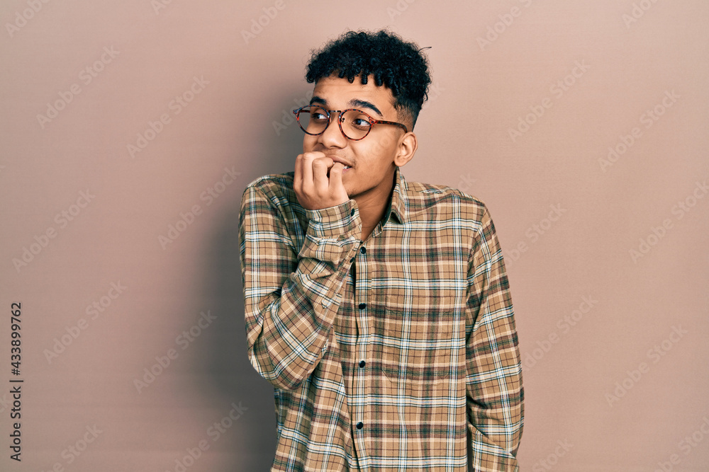 Young african american man wearing casual clothes and glasses looking stressed and nervous with hands on mouth biting nails. anxiety problem. Young african american man wearing casual clothes and glasses looking stressed and nervous with hands on mouth biting nails. anxiety problem.