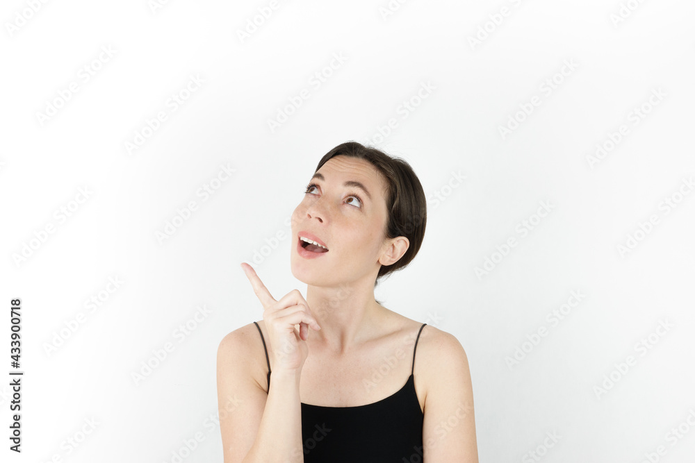 Young beautiful woman pointing up with fingers while thinking at white empty background Young beautiful woman pointing up with fingers while thinking at white empty background