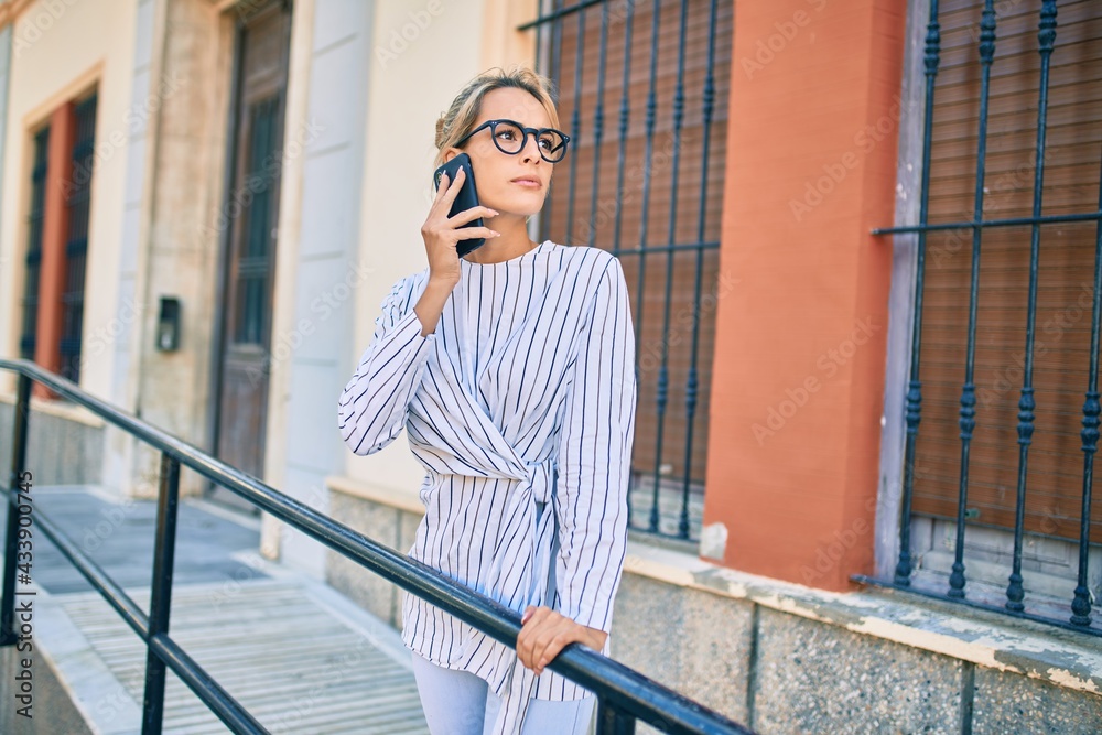 Young blonde businesswoman with serious expression talking on the smartphone at the city.