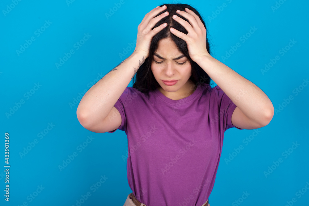 young beautiful tattooed girl wearing purple t-shirt holding head with hands, suffering from severe headache, pressing fingers to temples young beautiful tattooed girl wearing purple t-shirt holding head with hands, suffering from severe headache, pressing fingers to temples