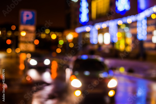 Rainy night in the parking shopping mall, the light from the headlights of a cars traveling towards. Defocused image