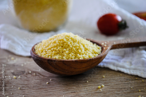 Raw couscous is sprinkled in a wooden spoon.