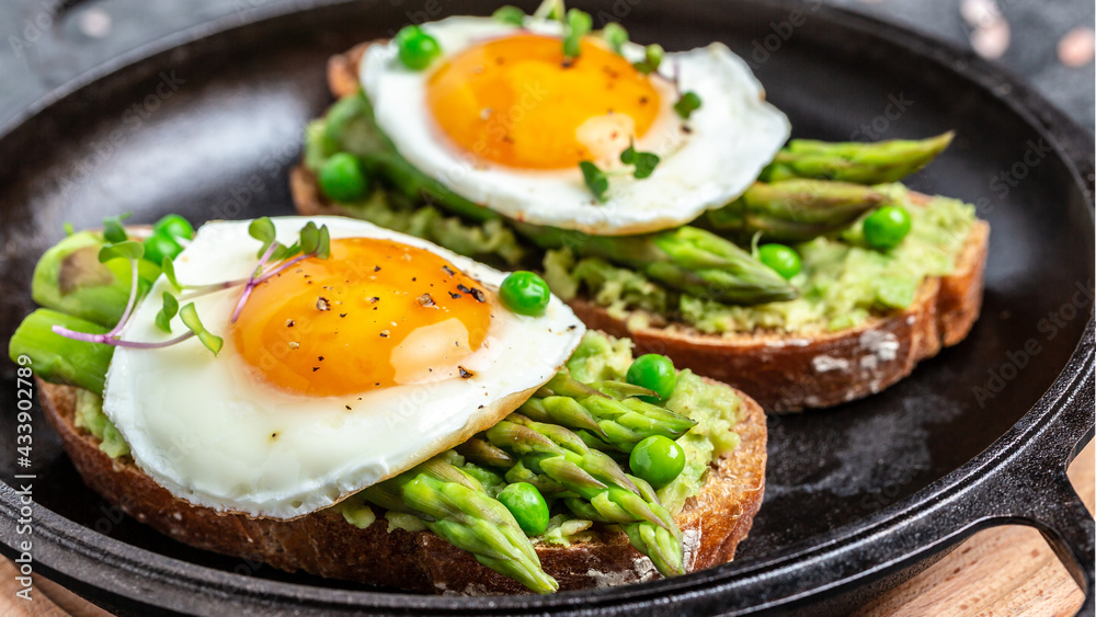 Tasty breakfast toasts with avocado, asparagus and fried egg. Healthy food, diet lunch concept, top view