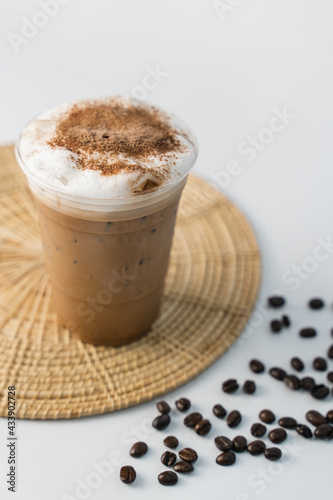 a glass of cappuccino coffee with sprinkled chocolate on milk foam sitting on rattan tray and coffee beans on the side