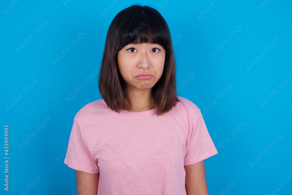young beautiful asian woman wearing pink t-shirt against blue wall crying desperate and depressed with tears on his eyes suffering pain and depression. Sad facial expression and emotion concept. young beautiful asian woman wearing pink t-shirt against blue wall crying desperate and depressed with tears on his eyes suffering pain and depression. Sad facial expression and emotion concept.