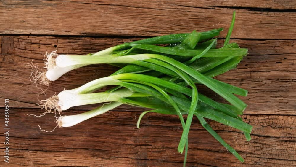 Falling fresh harvested spring onions on vintage wooden table. Super slow motion filmed on high speed cinematic camera at 1000 fps.