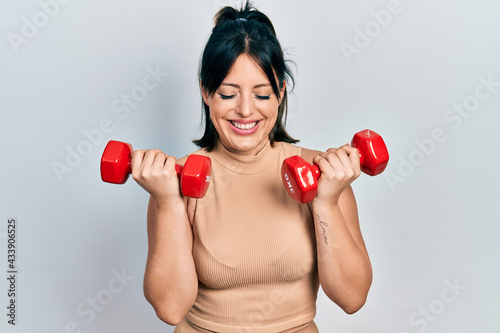 Young hispanic woman wearing sportswear using dumbbells smiling and laughing hard out loud because funny crazy joke.