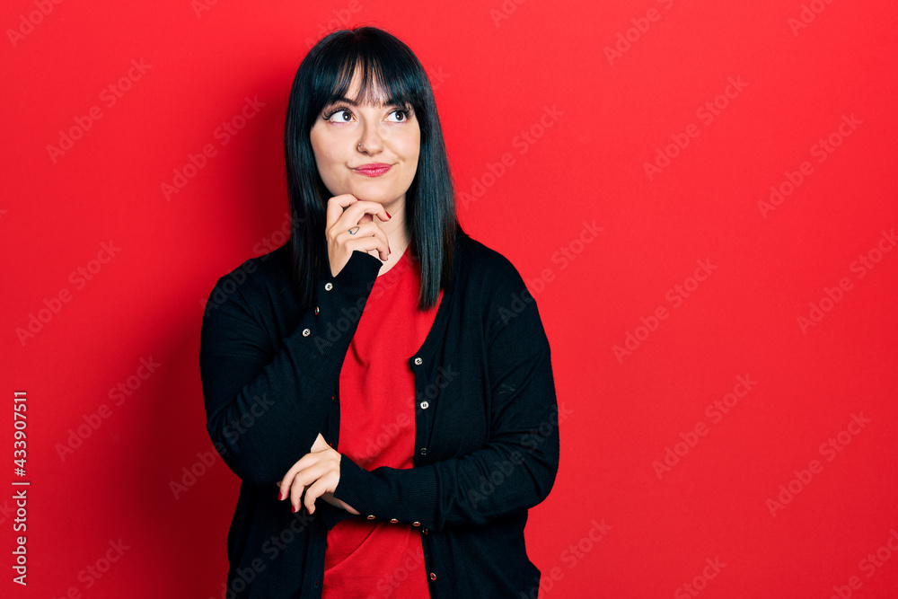 Young hispanic woman wearing casual clothes serious face thinking about question with hand on chin, thoughtful about confusing idea