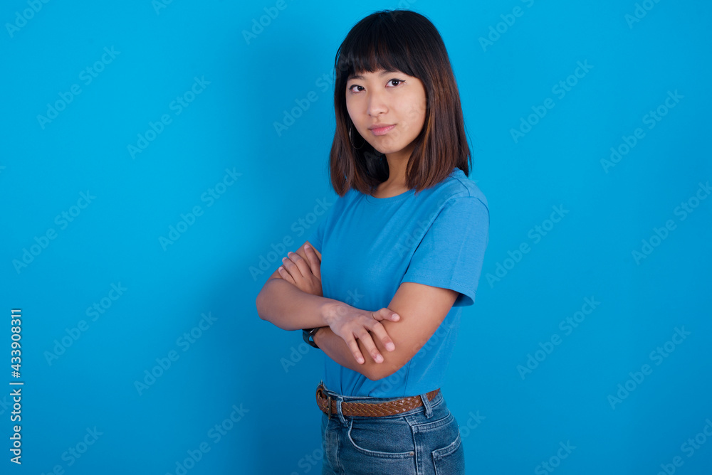 Portrait of young beautiful asian girl wearing blue t-shirt against blue background standing with folded arms and smiling Portrait of young beautiful asian girl wearing blue t-shirt against blue background standing with folded arms and smiling