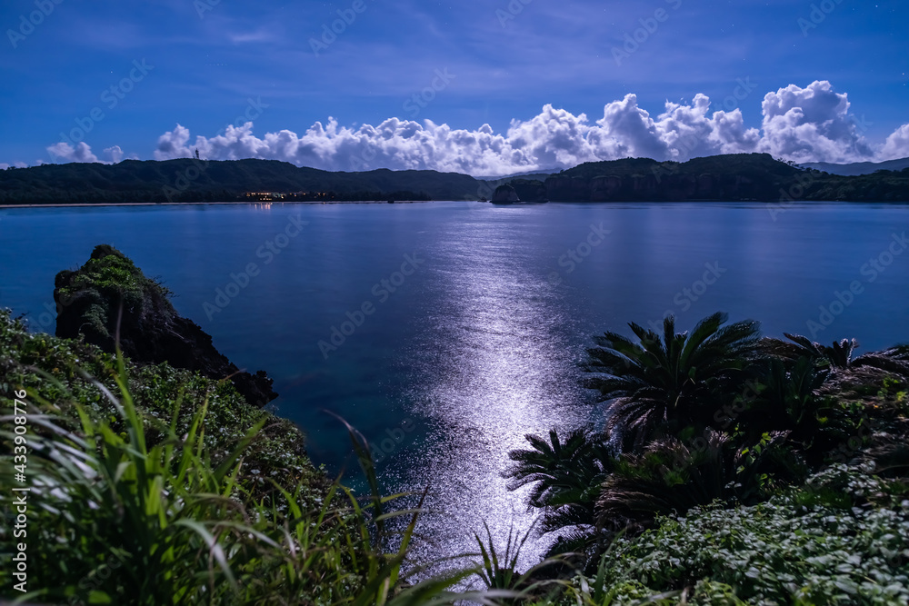 Spectacular seascape view. Amazing reflection of the full moon over the sea in long exposure. Mountain, clouds and vegetation compounding the night scene. Iriomote Island.