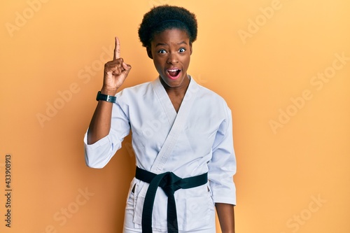 Young african american girl wearing karate kimono and black belt pointing finger up with successful idea. exited and happy. number one.