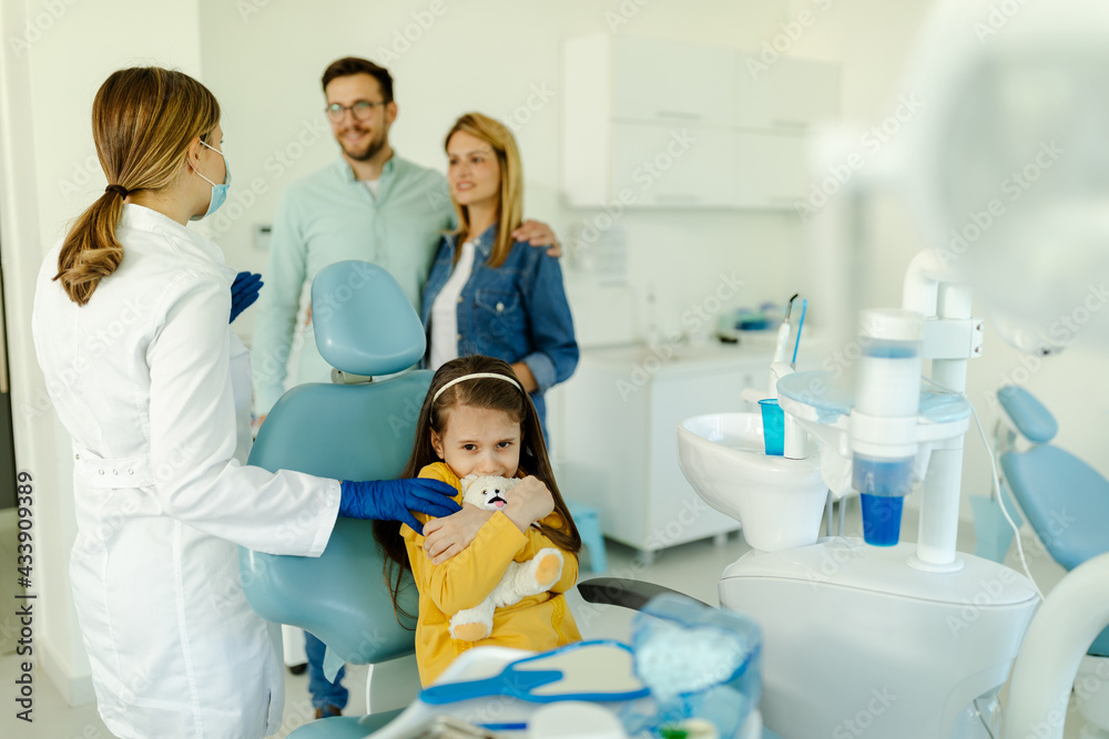 A frightened girl hugged her toy while sitting in a dental chair. A frightened girl hugged her toy while sitting in a dental chair.