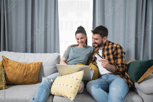 Young happy couple with laptop computer sitting at home ordering and online shopping a new furniture and kitchen equipment for their apartment cause they start living together  photo