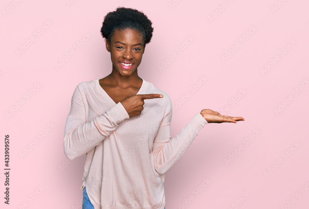 Young african american girl wearing casual clothes amazed and smiling to the camera while presenting with hand and pointing with finger. Young african american girl wearing casual clothes amazed and smiling to the camera while presenting with hand and pointing with finger.