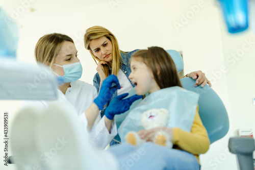 Young girl having check up at dentists surgery with mother. Focus on worried mother.