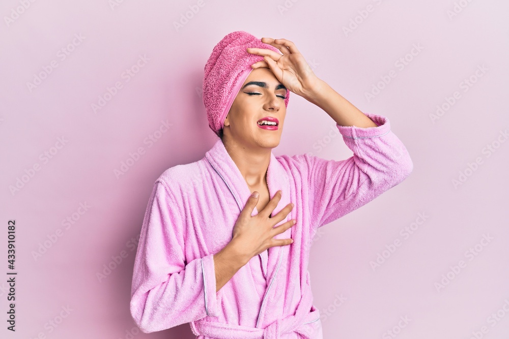 Young man wearing woman make up wearing shower towel on head and bathrobe touching forehead for illness and fever, flu and cold, virus sick Young man wearing woman make up wearing shower towel on head and bathrobe touching forehead for illness and fever, flu and cold, virus sick