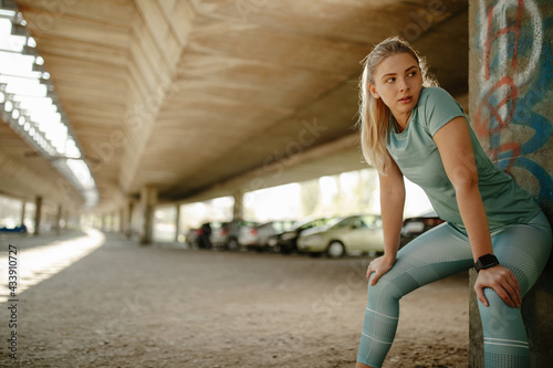 Young blonde woman wearing sports wear leaning a wall looking away.