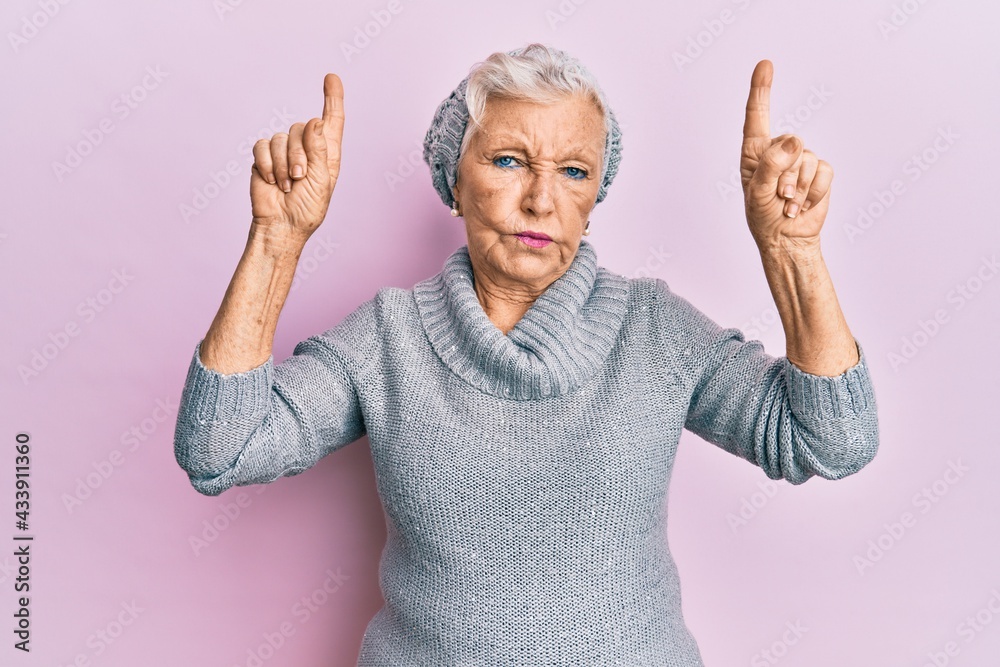 Senior grey-haired woman pointing up with fingers skeptic and nervous, frowning upset because of problem. negative person. Senior grey-haired woman pointing up with fingers skeptic and nervous, frowning upset because of problem. negative person.