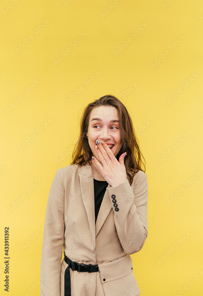Beautiful woman in smart casual clothes looks to the side and smiles covering her mouth with her hand on a yellow background, vertical. Beautiful woman in smart casual clothes looks to the side and smiles covering her mouth with her hand on a yellow background, vertical.