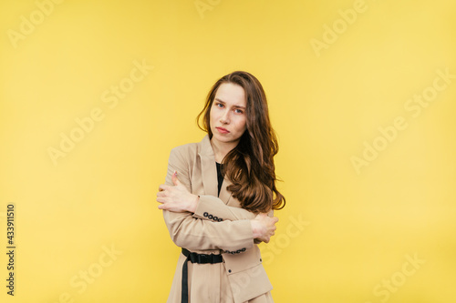 Frozen woman in a suit isolated on a yellow background, hugged herself and looked at the camera with a sad face.