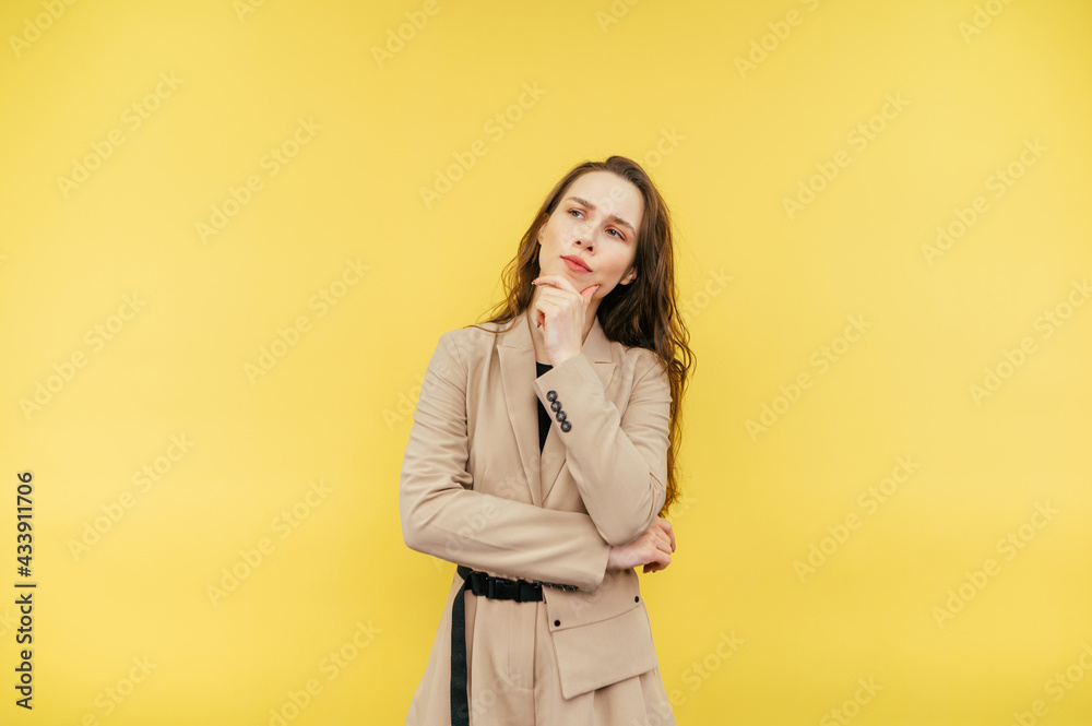 Portrait of a pensive lady in a beige suit on a yellow background, looking away with a serious face and thinking. Portrait of a pensive lady in a beige suit on a yellow background, looking away with a serious face and thinking.