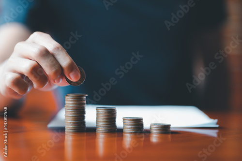 Closeup man hands. Businessman holding coin to place on stack of coins placed on the table. Accounting, Financial investment, saving money for future growth concept