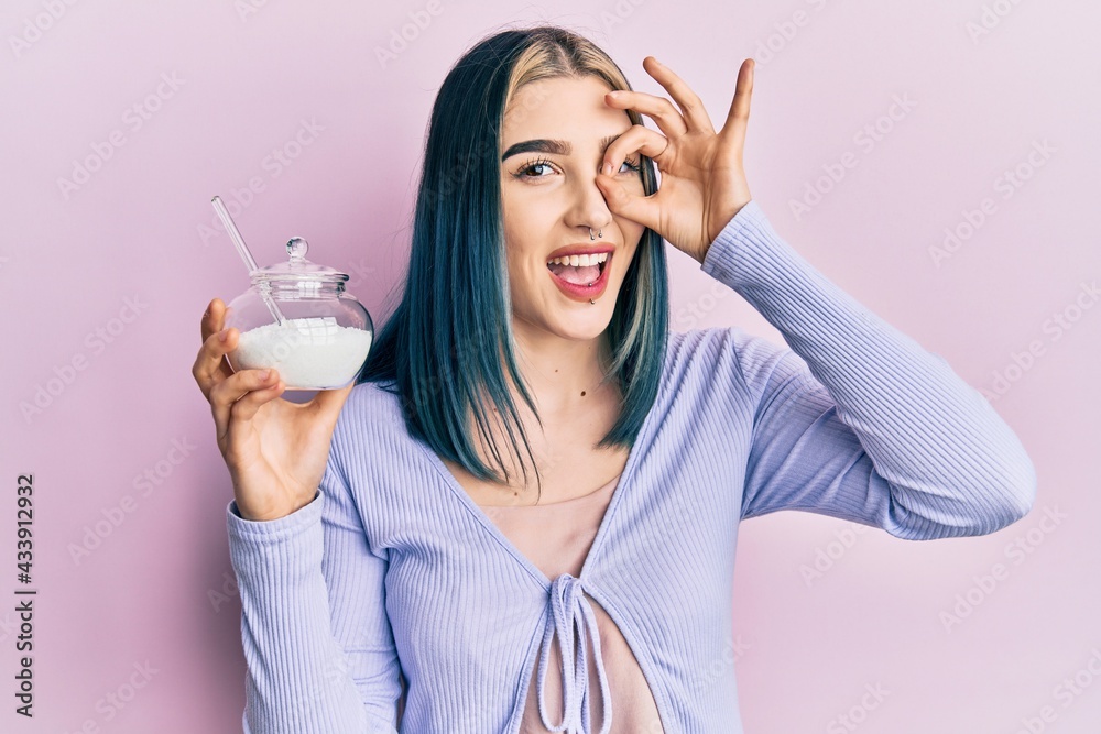 Young modern girl holding bowl with sugar smiling happy doing ok sign with hand on eye looking through fingers Young modern girl holding bowl with sugar smiling happy doing ok sign with hand on eye looking through fingers