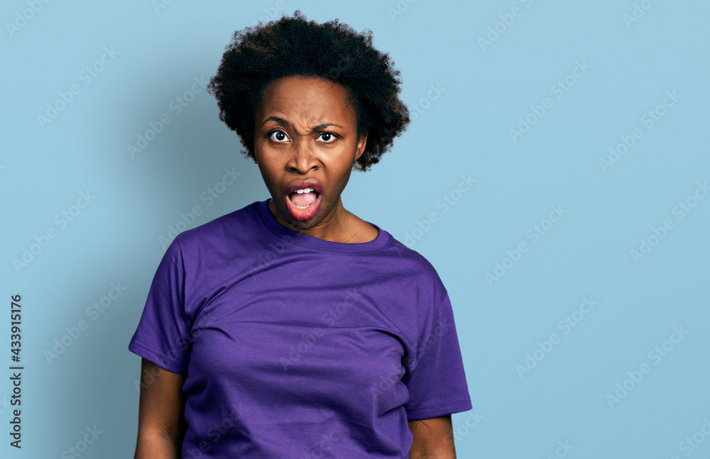African american woman with afro hair wearing casual purple t shirt in shock face, looking skeptical and sarcastic, surprised with open mouth African american woman with afro hair wearing casual purple t shirt in shock face, looking skeptical and sarcastic, surprised with open mouth