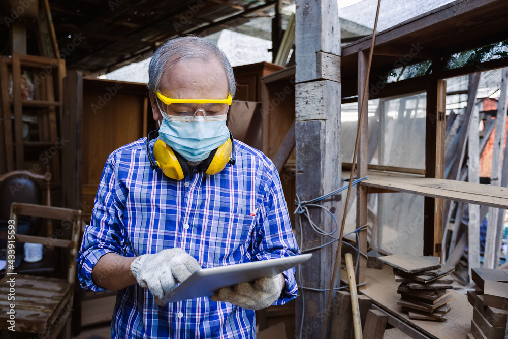 asian senior man carpenter wear headphone using tablet standing in workplace. carpenter concept.