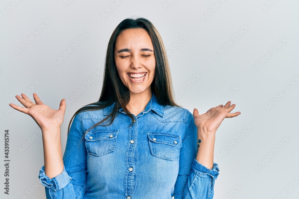 Young hispanic woman wearing casual denim jacket celebrating mad and crazy for success with arms raised and closed eyes screaming excited. winner concept Young hispanic woman wearing casual denim jacket celebrating mad and crazy for success with arms raised and closed eyes screaming excited. winner concept