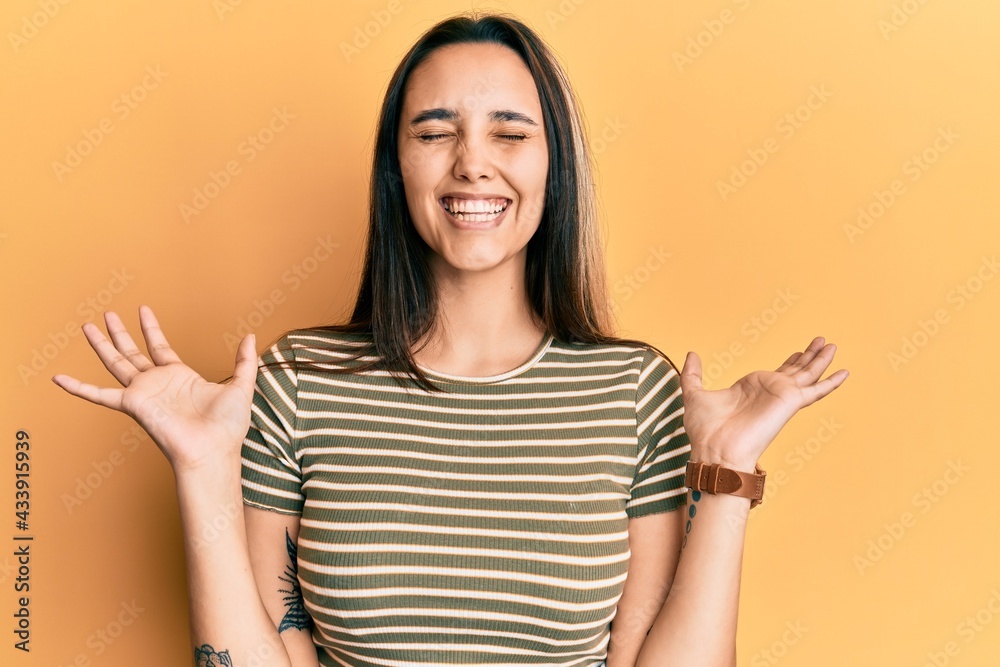 Young hispanic woman wearing casual striped t shirt celebrating mad and crazy for success with arms raised and closed eyes screaming excited. winner concept Young hispanic woman wearing casual striped t shirt celebrating mad and crazy for success with arms raised and closed eyes screaming excited. winner concept
