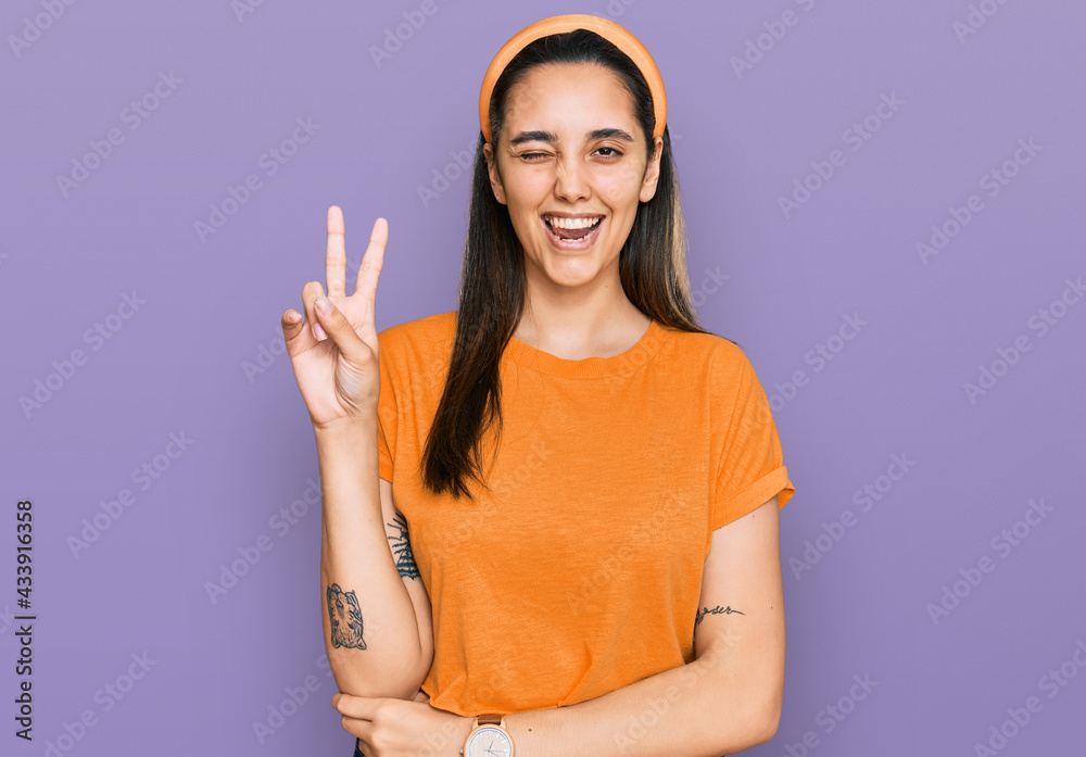 Young hispanic woman wearing casual clothes smiling with happy face winking at the camera doing victory sign with fingers. number two. Young hispanic woman wearing casual clothes smiling with happy face winking at the camera doing victory sign with fingers. number two.