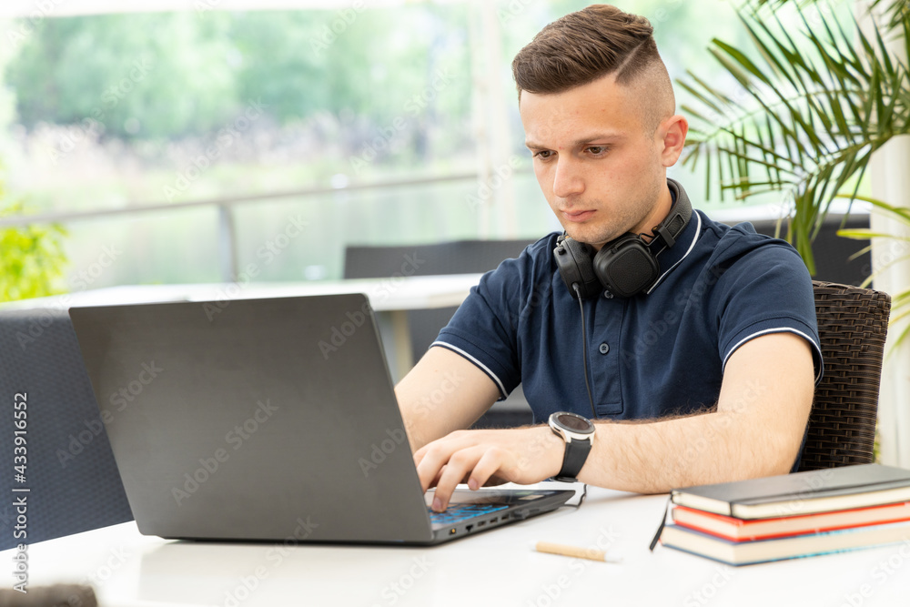 Young man writes text in a laptop while sitting at a table in a co working cafe. Male freelancer working remotely on a project. Young man writes text in a laptop while sitting at a table in a co working cafe. Male freelancer working remotely on a project.