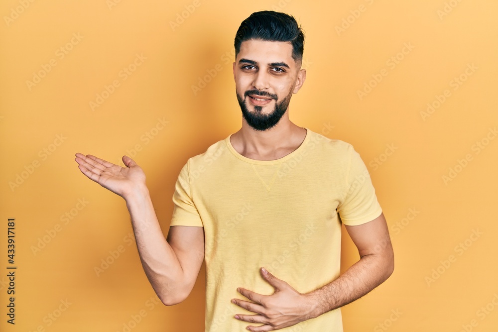 Handsome man with beard wearing casual yellow t shirt smiling cheerful presenting and pointing with palm of hand looking at the camera. Handsome man with beard wearing casual yellow t shirt smiling cheerful presenting and pointing with palm of hand looking at the camera.