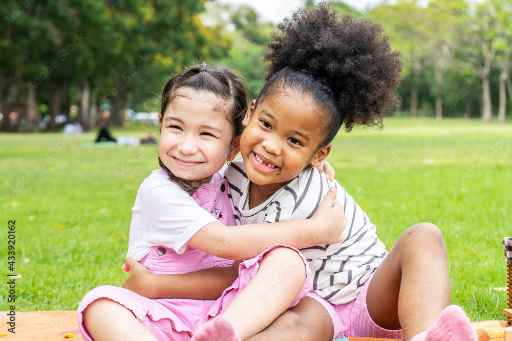 Two African American cheerful little girl sitting on the mat and hugging each other with love in the garden Two African American cheerful little girl sitting on the mat and hugging each other with love in the garden