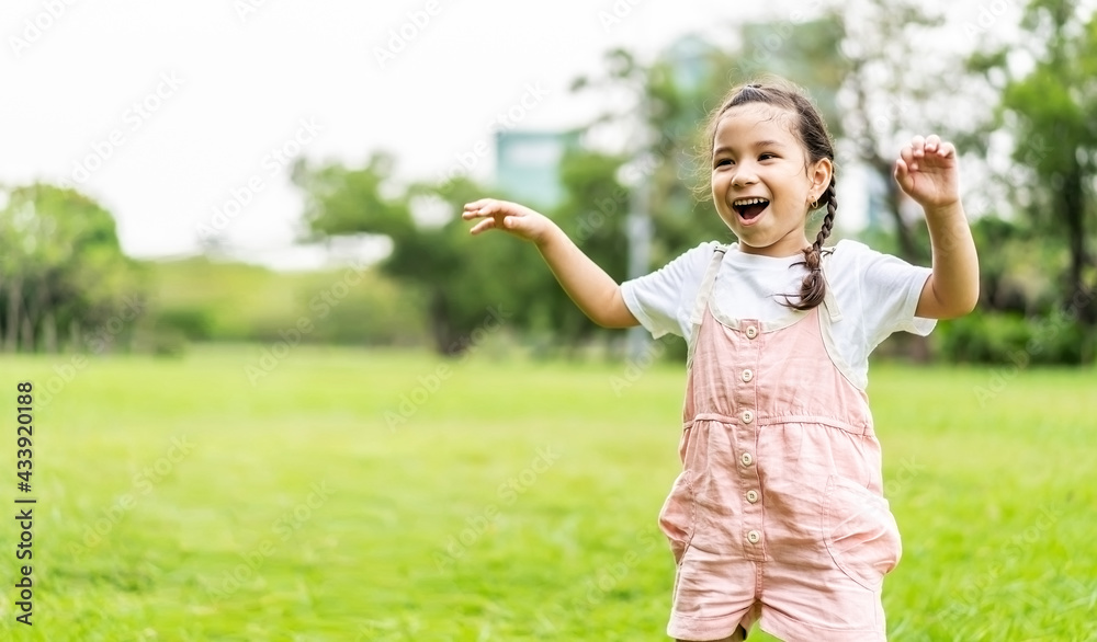 Portrait of happy pretty child girl smiling and raises her hand while standing in the park, Positive female kid enjoying warm day in fall park Portrait of happy pretty child girl smiling and raises her hand while standing in the park, Positive female kid enjoying warm day in fall park