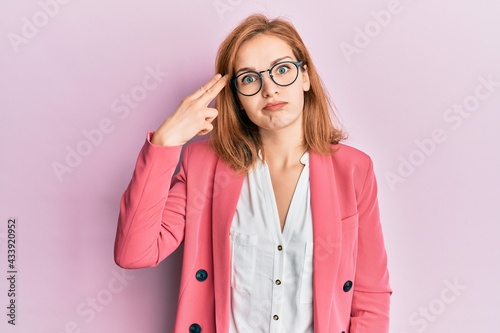 Obraz na plátne Young caucasian woman wearing business style and glasses shooting and killing oneself pointing hand and fingers to head like gun, suicide gesture