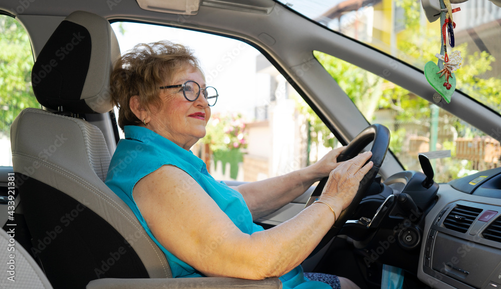 Obraz premium Beautiful lady in a blue shirt in her 70s is driving a car
