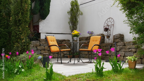 Fototapeta Naklejka Na Ścianę i Meble -  Gartenterrasse im Frühling umgeben von Tulpen, Funkien, Säulenbaum und Zypressen