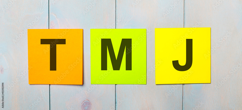 Three colored stickers with the text ADA Americans with TMJ on a light blue wooden background Three colored stickers with the text ADA Americans with TMJ on a light blue wooden background