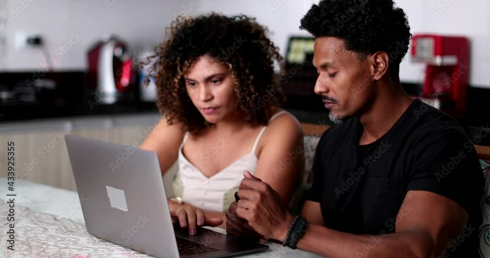 Candid African couple using laptop computer at home kitchen Candid African couple using laptop computer at home kitchen