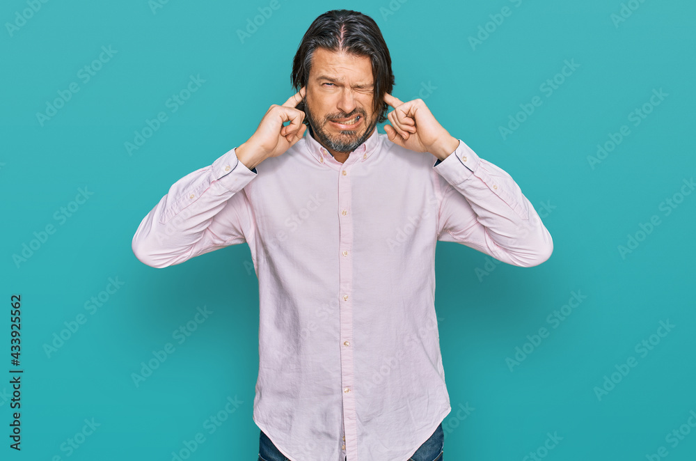 Middle age handsome man wearing business shirt covering ears with fingers with annoyed expression for the noise of loud music. deaf concept. Middle age handsome man wearing business shirt covering ears with fingers with annoyed expression for the noise of loud music. deaf concept.