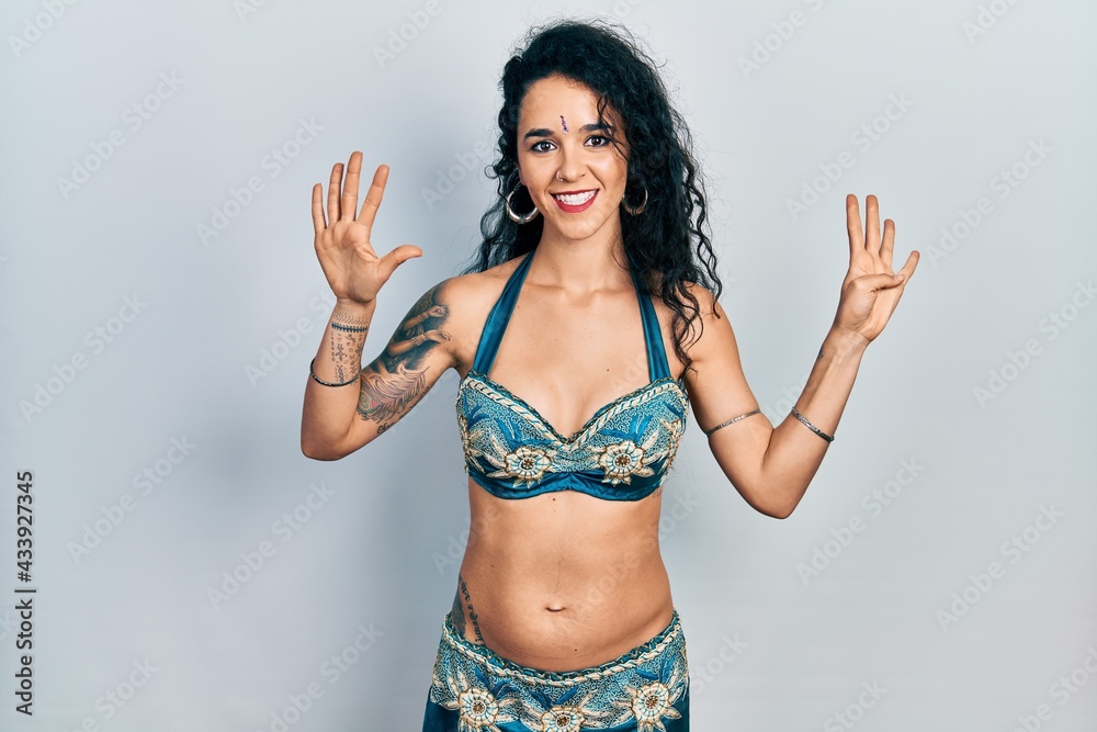 Fototapeta premium Young woman wearing bindi and traditional belly dance clothes showing and pointing up with fingers number nine while smiling confident and happy.
