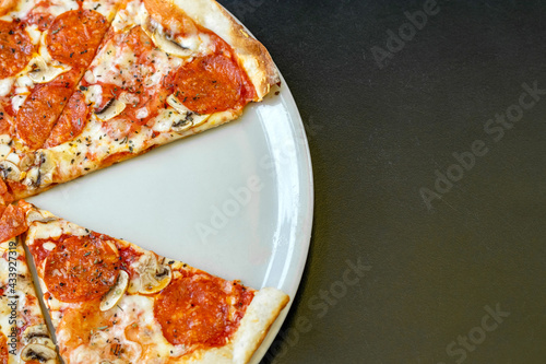 Pizza top view with mozzarella, herbs, mushrooms and tomatoes with missing piece on dark background.