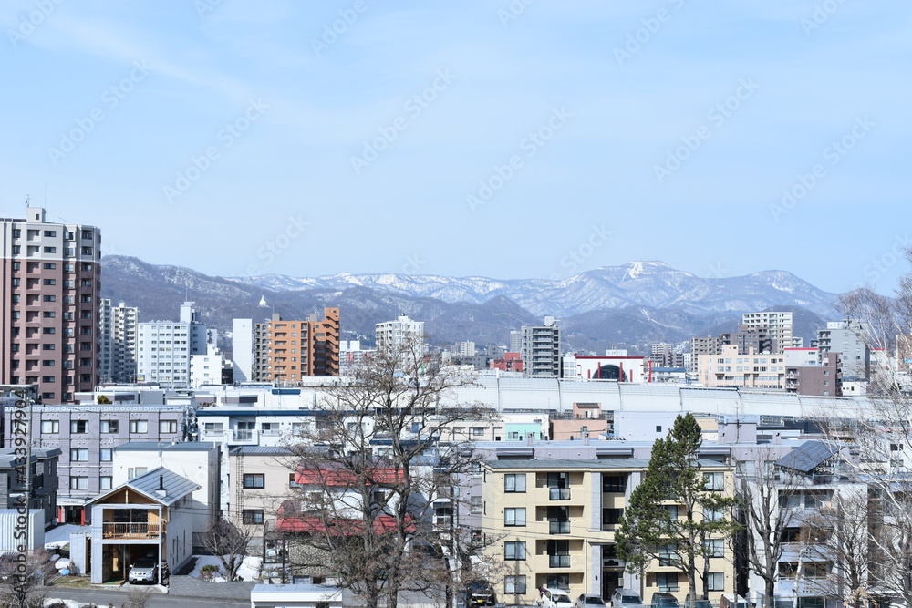 The early spring townscape of Sapporo from the Hiragishi Takadai with white mountains in Sapporo Japan on April 24 2021