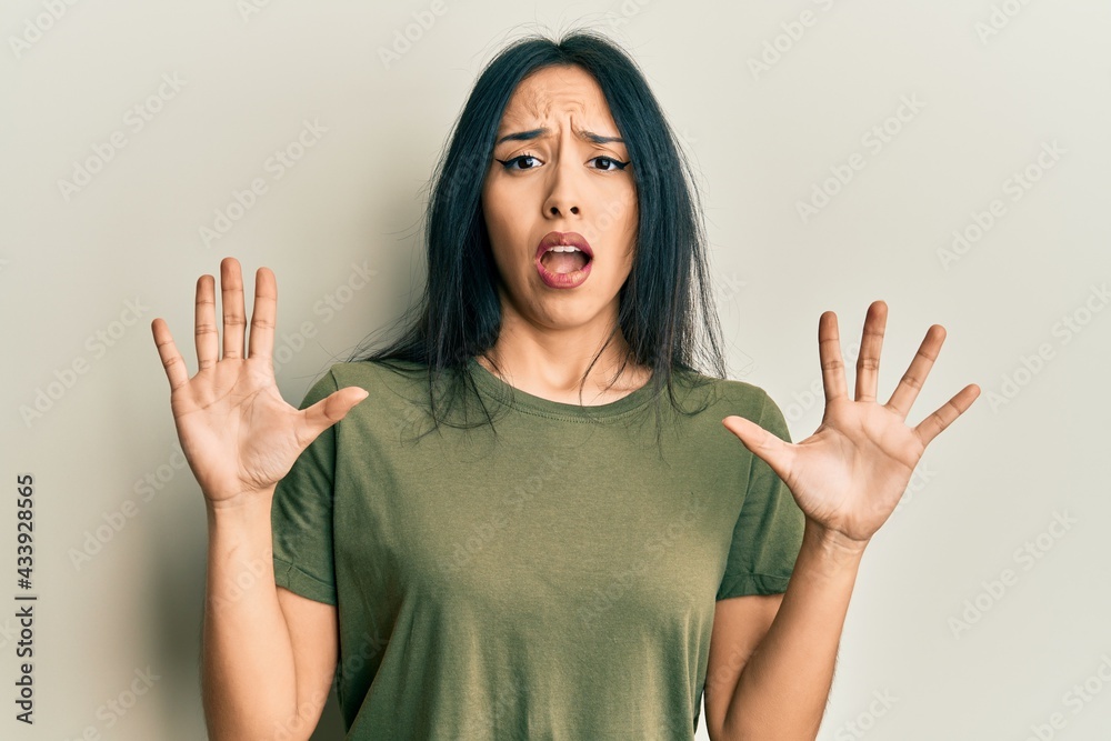 Young hispanic girl wearing casual t shirt afraid and terrified with fear expression stop gesture with hands, shouting in shock. panic concept.