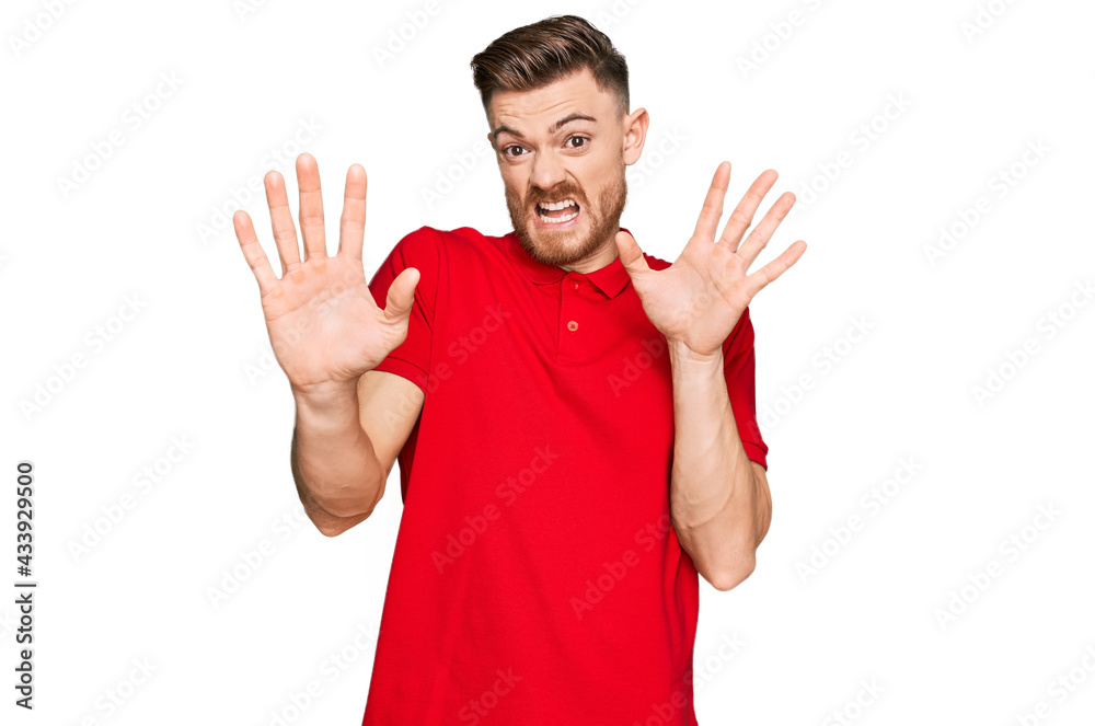 Young redhead man wearing casual clothes afraid and terrified with fear expression stop gesture with hands, shouting in shock. panic concept. Young redhead man wearing casual clothes afraid and terrified with fear expression stop gesture with hands, shouting in shock. panic concept.