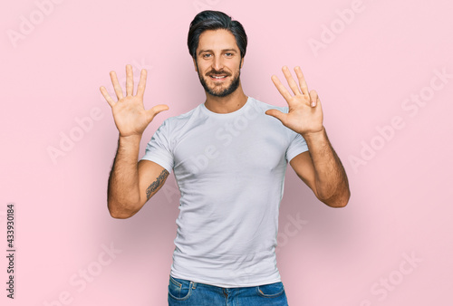 Young hispanic man wearing casual white t shirt showing and pointing up with fingers number nine while smiling confident and happy.